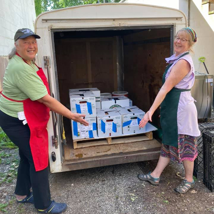 two workers show off meals packed in boxes in a truck for delivery to the community