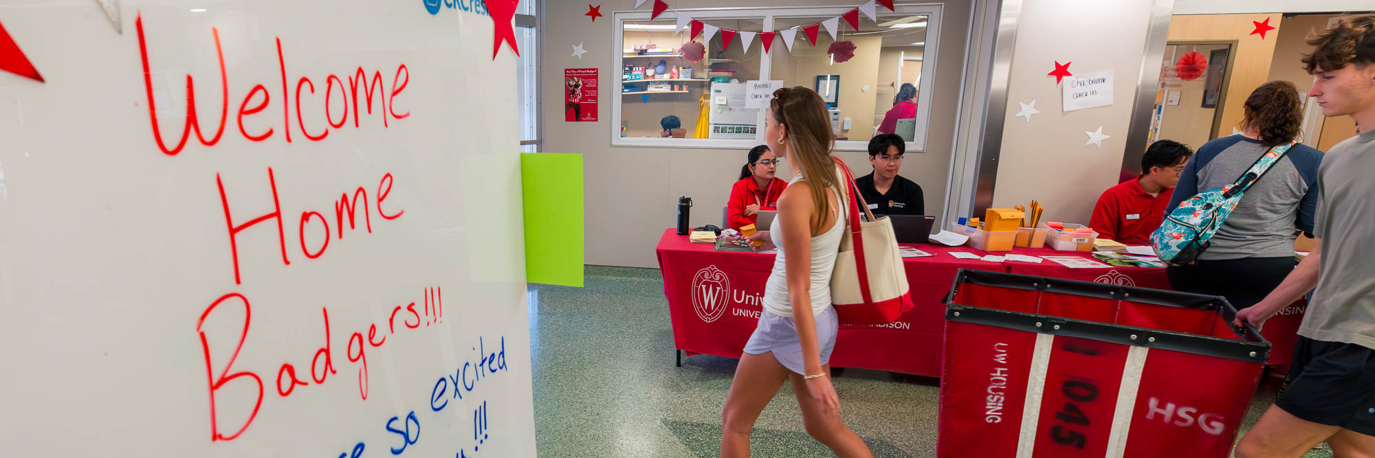 A sign reading "Welcome Home Badgers!!!" in the foreground and students moving a cart in the background
