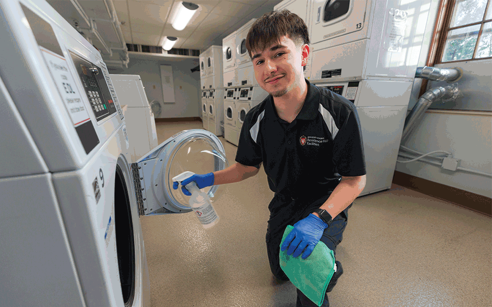 A student cleans a washing machine in Waters Residence Hall with text overlaid reading "Build character and skills working in a student job"