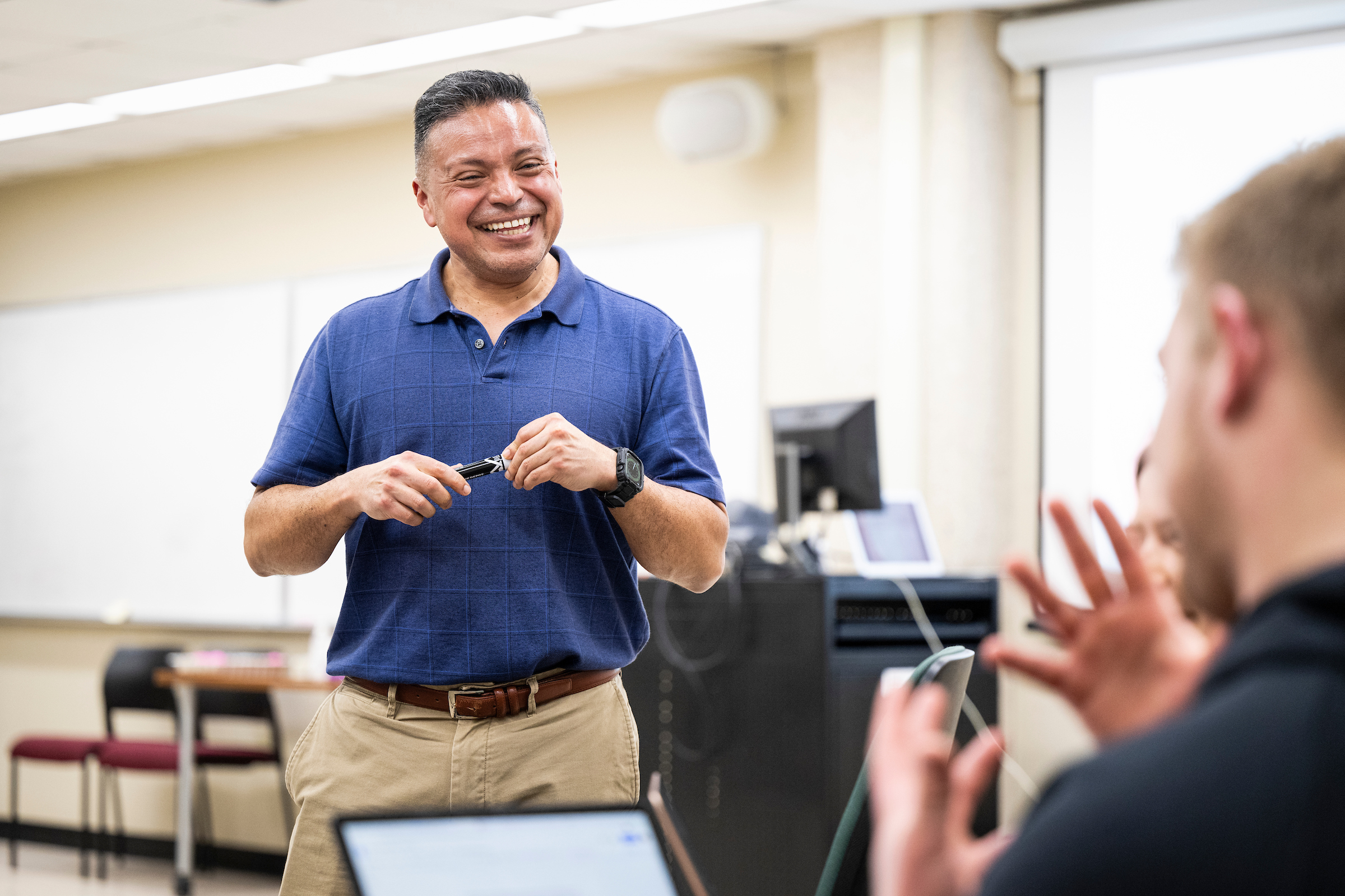 Photo of Diego Román, assistant professor of bilingual/bicultural education in the Department of Curriculum and Instruction in the School of Education, standing and speaking to an undergraduate student in one of his classes.