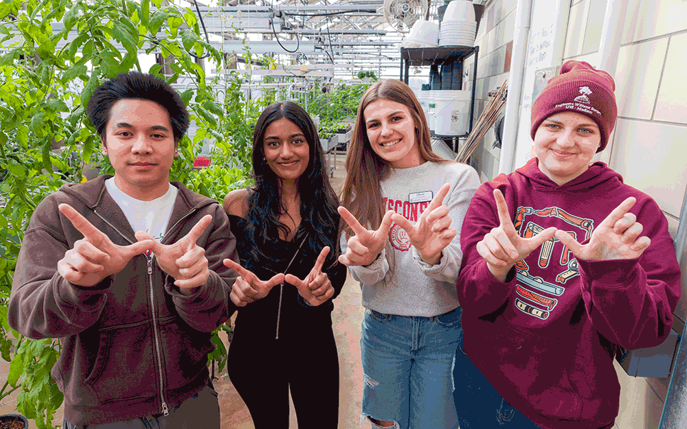A group of students pose for a photo in Leopold Residence Hall's greenhouse while making the letter "W" with their hands. Text is overlaid reading "Make a large university smaller & more intimate."