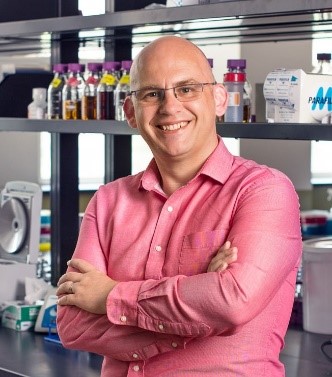 J.P. van Pijkeren in glasses and pink shirt standing in front of lab bench