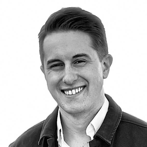 Image of Devin Kennedy in black and white. He is smiling and wearing a white collard shirt and a dark jacket.