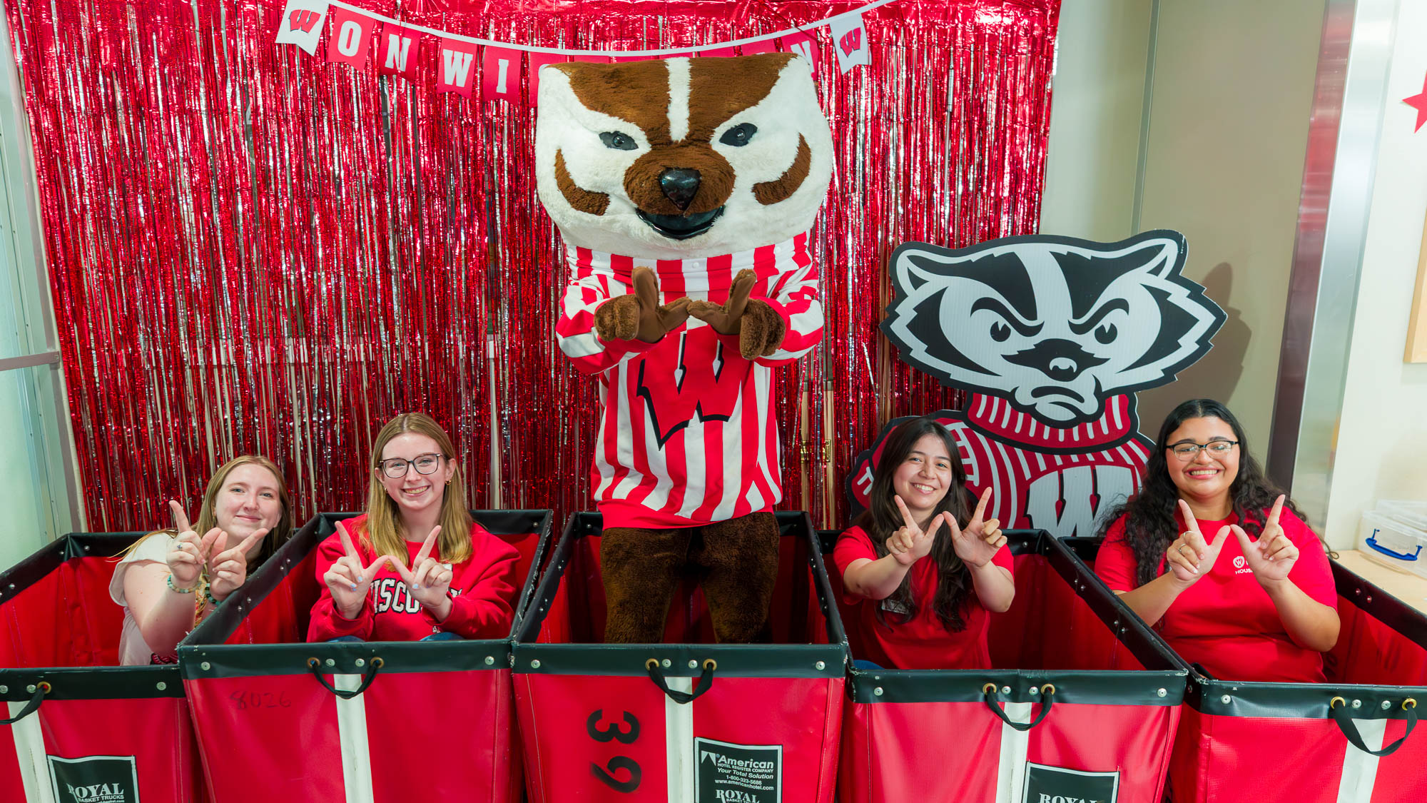 Bucky Badger and students in move-in carts make the letter "W" with their hands