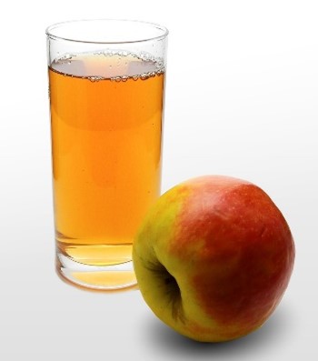 Photograph of a clear glass filled with amber-colored apple juice next to a red and green apple. 