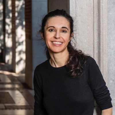 Image of Esther Fernandez inside a building. He is wearing a black shirt and has her dark hair in a ponytail. She is smiling.