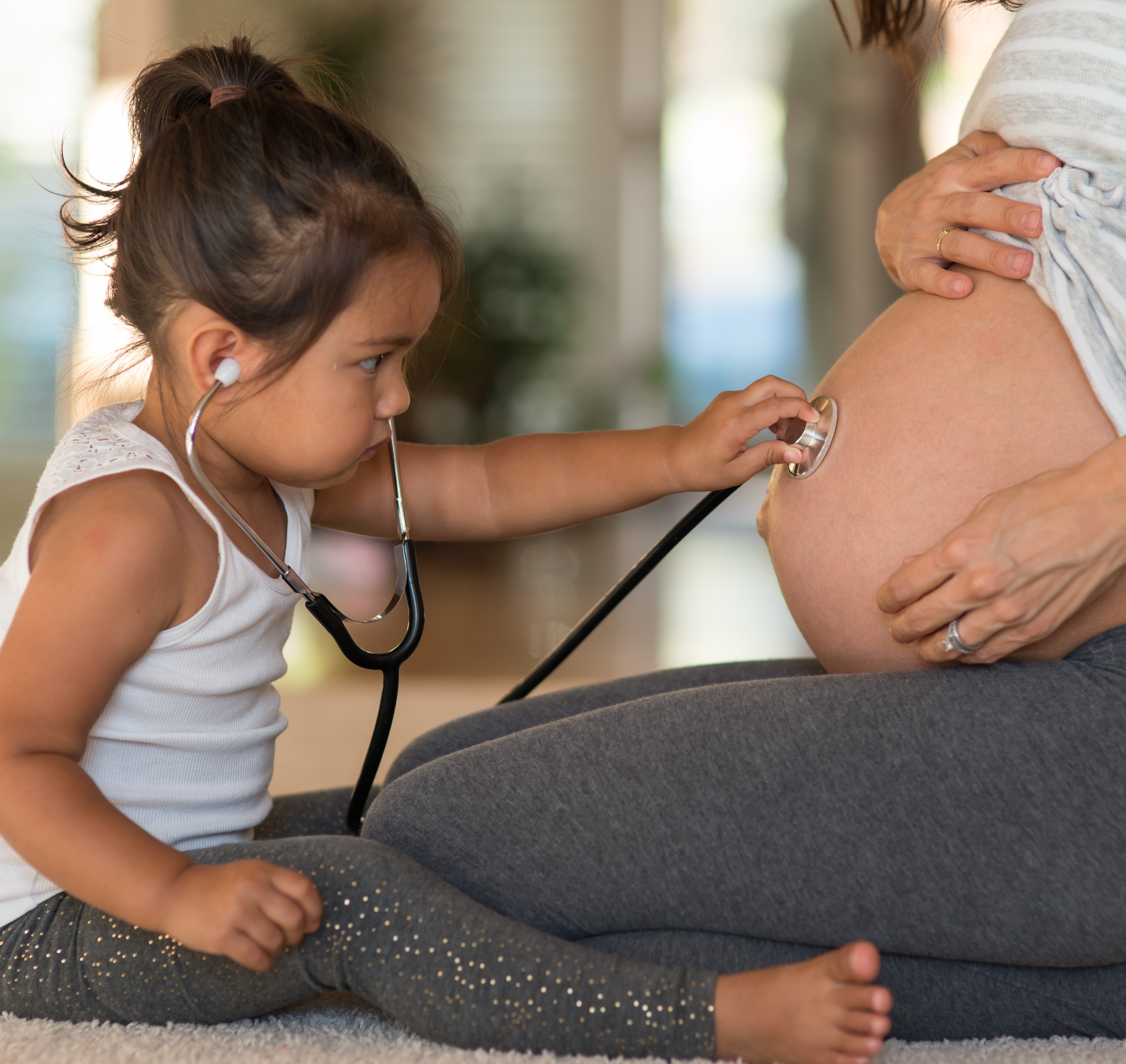 little girl holds stethoscope to pregnant mother's belly